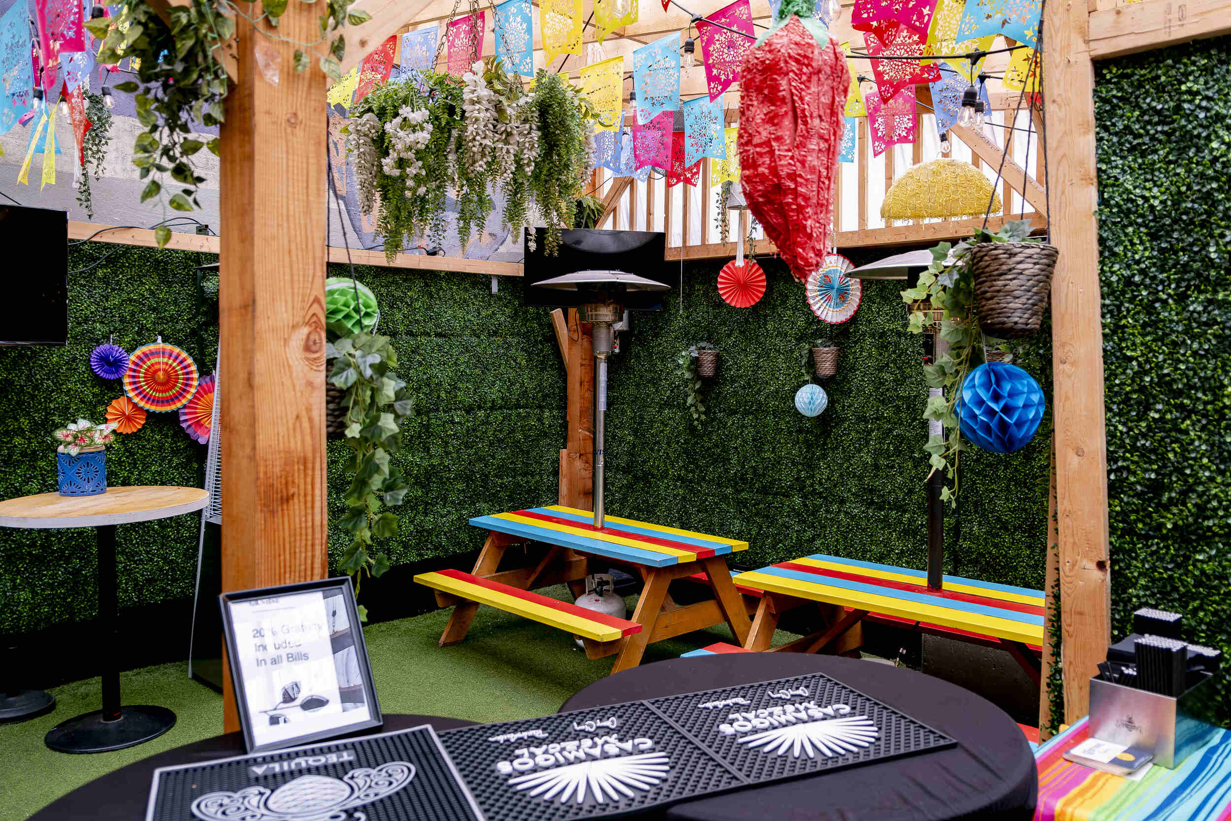 Colourful back Hideaway patio event space at The Pawn Shop YVR, downtown Vancouver. Vibrant papel picado, green ivy, and a multi-coloured picnic table.